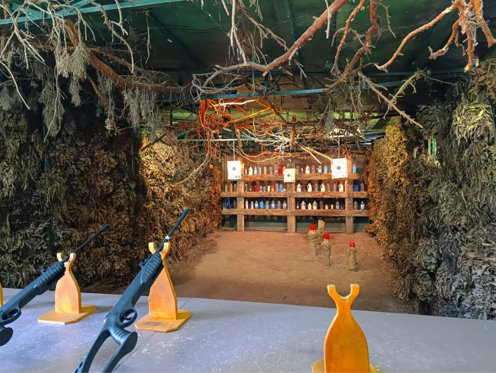 Заснеженная страйкбольная арена в лесу с мишенями, окружённая деревьями и ветками, внутри устроена имитация леса для активного отдыха и игр.