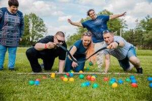 картинка группы людей, участвующих в командной игре на зеленом лугу с разноцветными мячами, в солнечную погоду, на природе, активный отдых, дружеское общение, отдых в Подмосковье, ВЕ Art Resort.